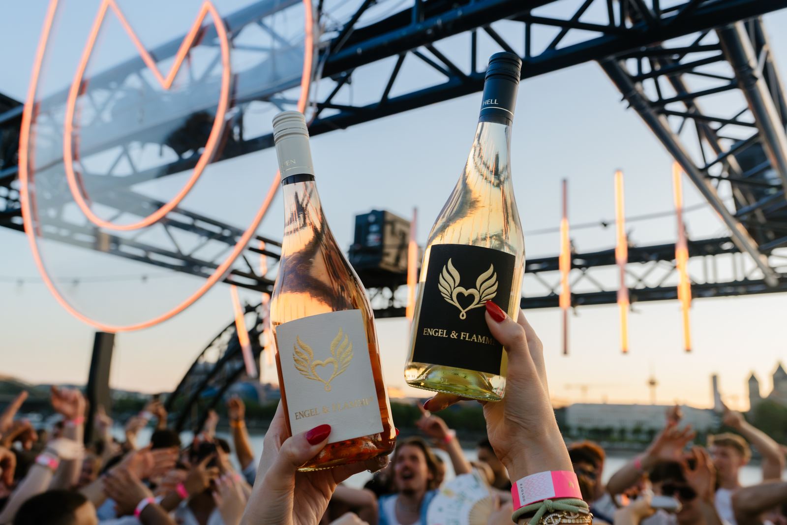 HEAVEN Rosé und HELL Weißwein von Engel & Flamme werden bei einem Sommerabend in die Luft gehalten, dahinter die Neon-Flamme
